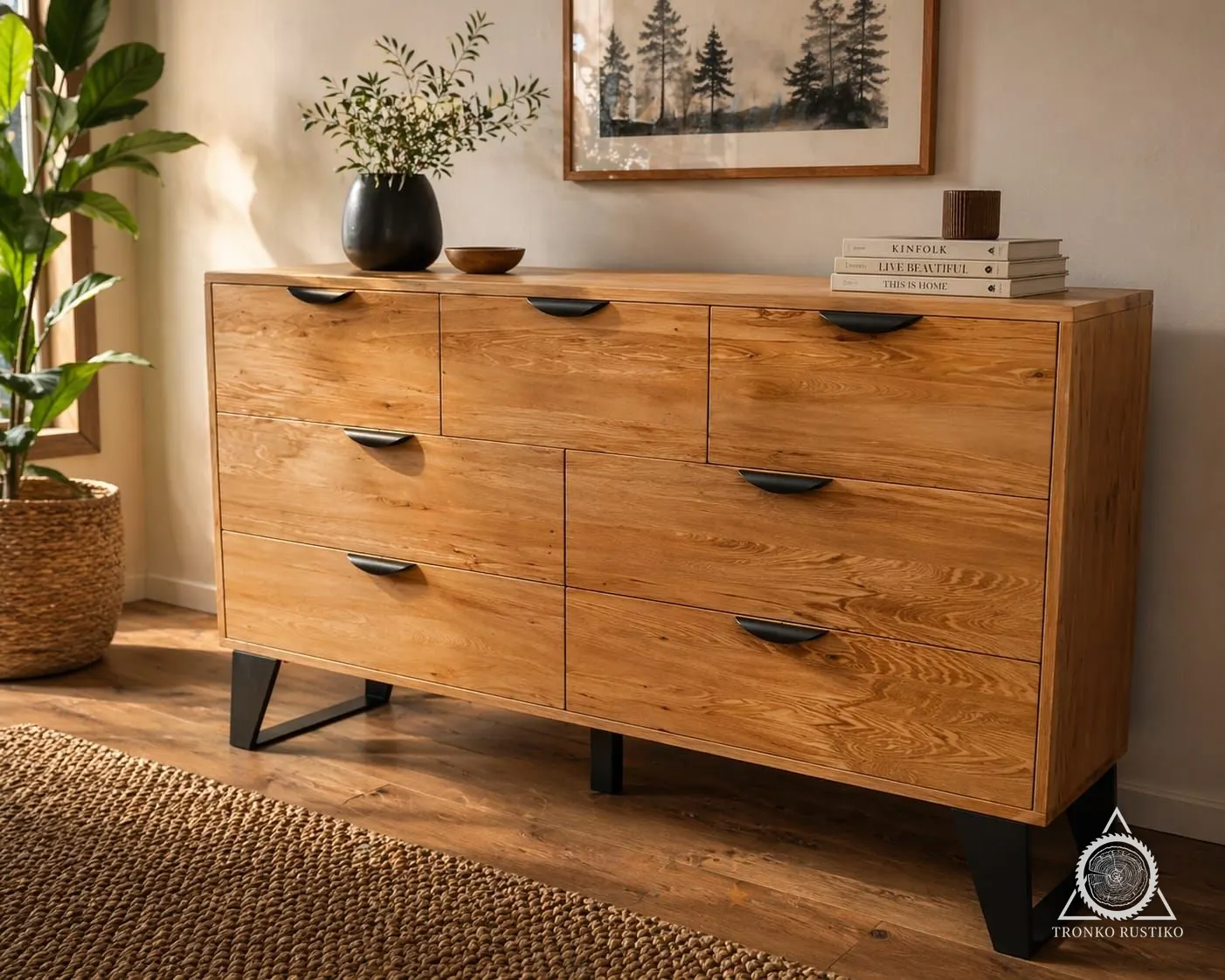 Cómoda de madera clara con siete cajones, tiradores negros curvos y patas de fierro negro.