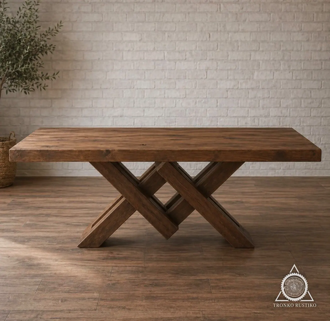 Mesa de comedor de madera con base central de piezas inclinadas y entrecruzadas, frente a un muro de ladrillo blanco.