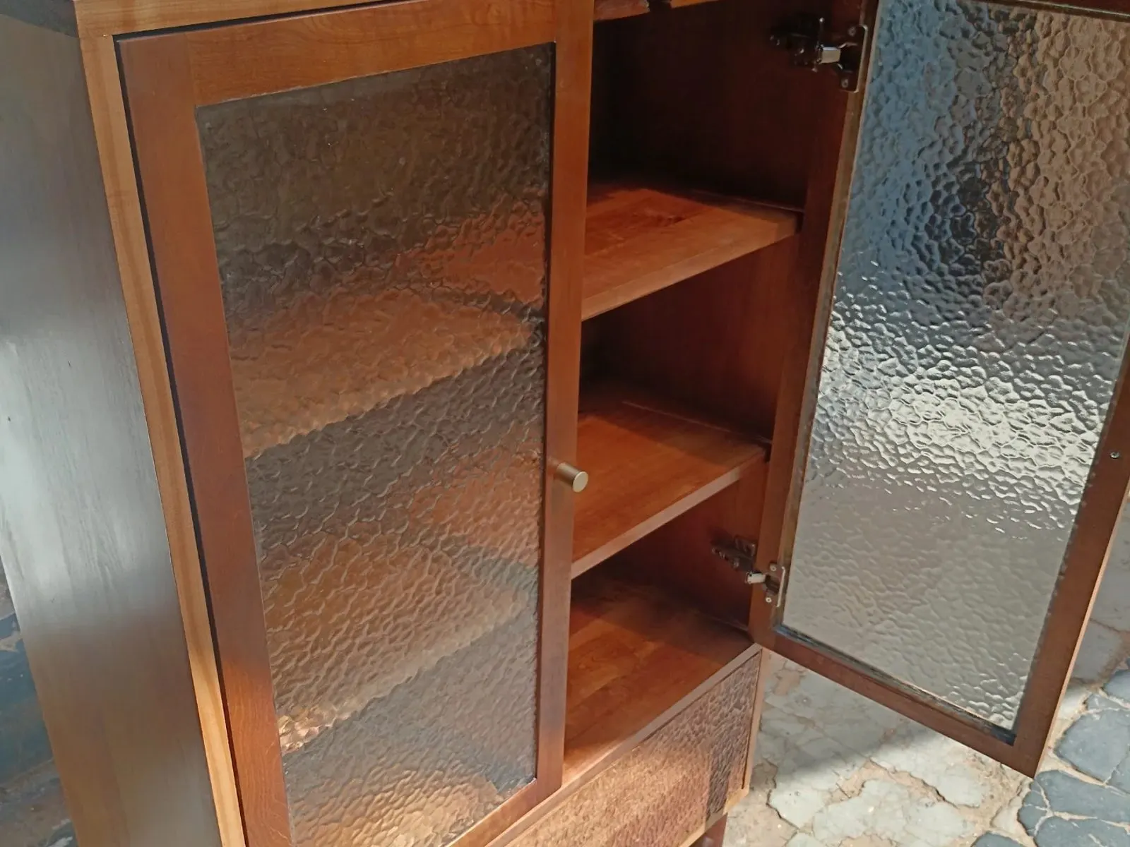 Vitrina de madera con la puerta de vidrio martelé abierta.