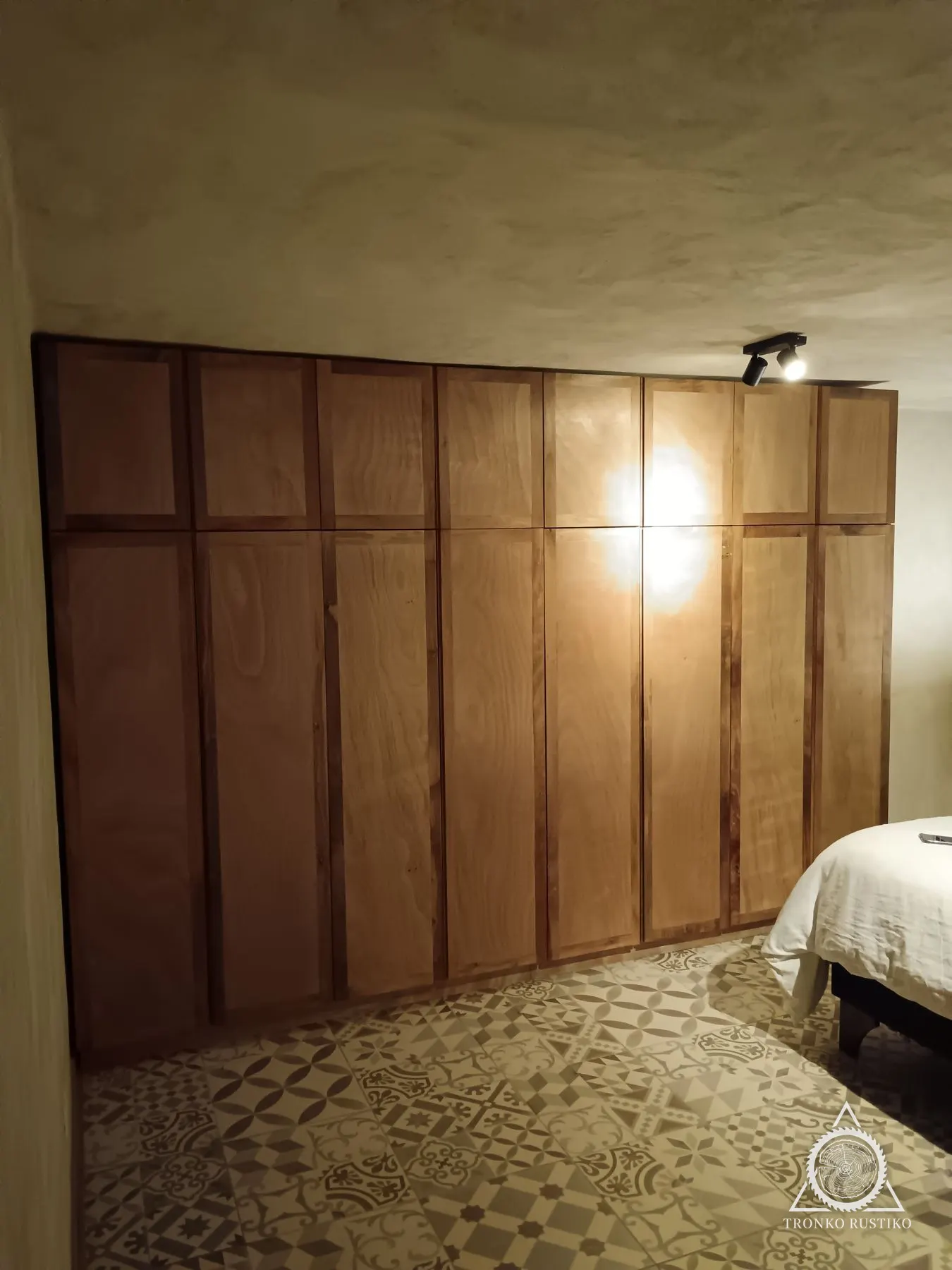 Clóset de piso a cielo con puertas de madera rojiza enchapada, junto a una cama.