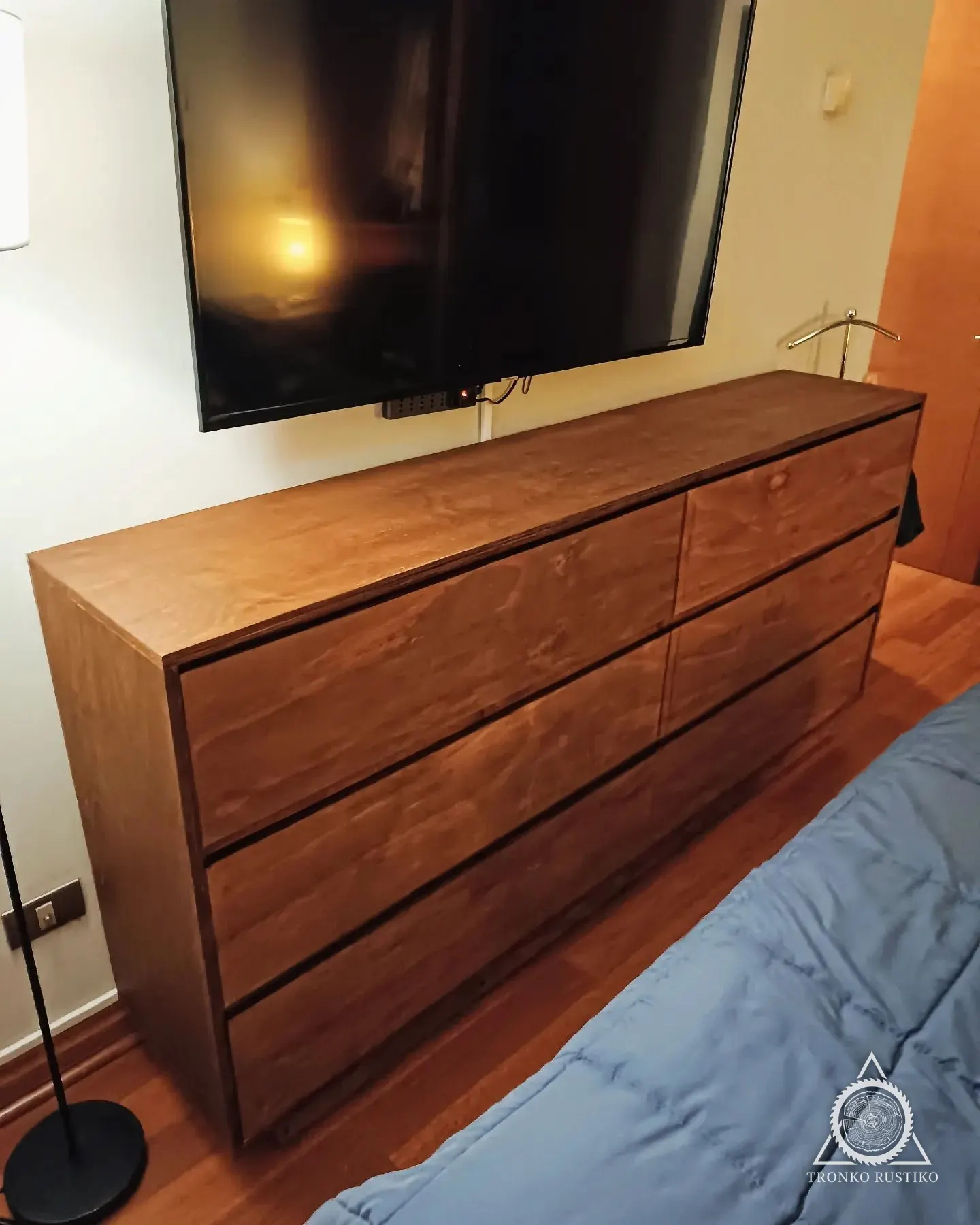 Cómoda baja y larga de madera, sin tiradores a la vista, bajo un televisor.