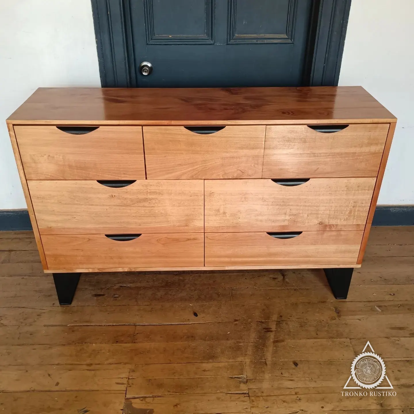 Cómoda de madera rojiza con seis cajones de tiradores rebajados y base metálica negra.