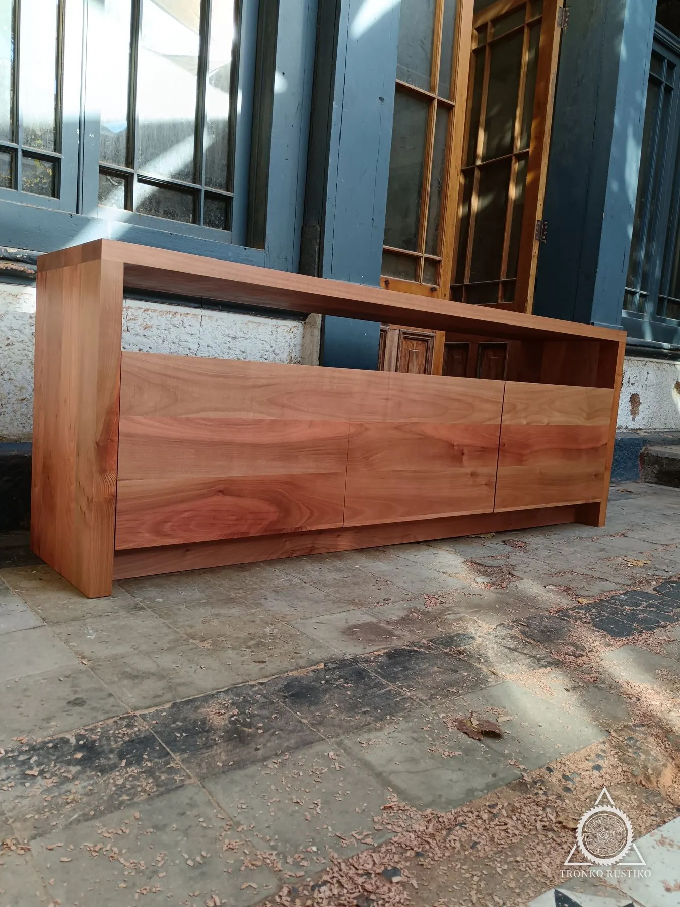 Rack de madera rojiza con compartimentos cerrados y un marco superior que forma un nicho para equipos.