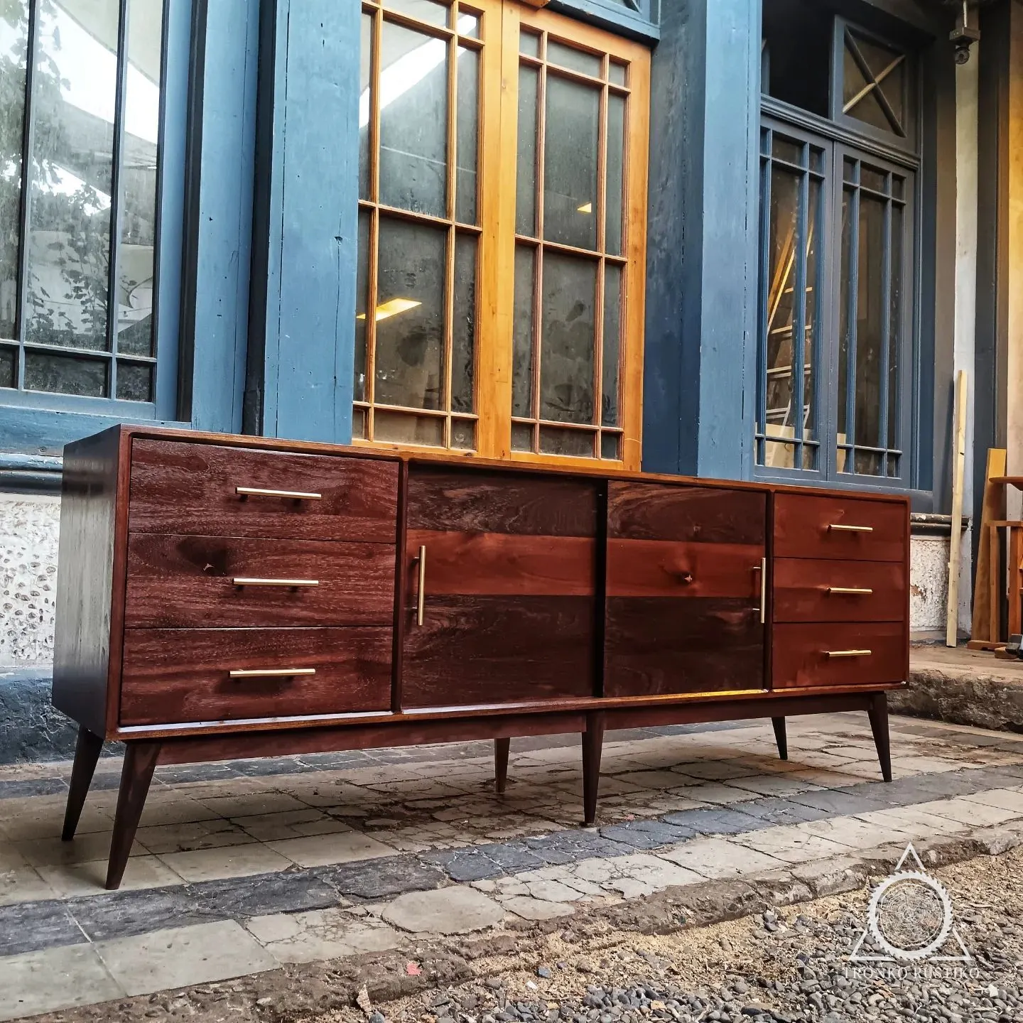 Buffet de madera oscura de estilo mid-century, con cajones laterales, puertas correderas al centro y patas cónicas.
