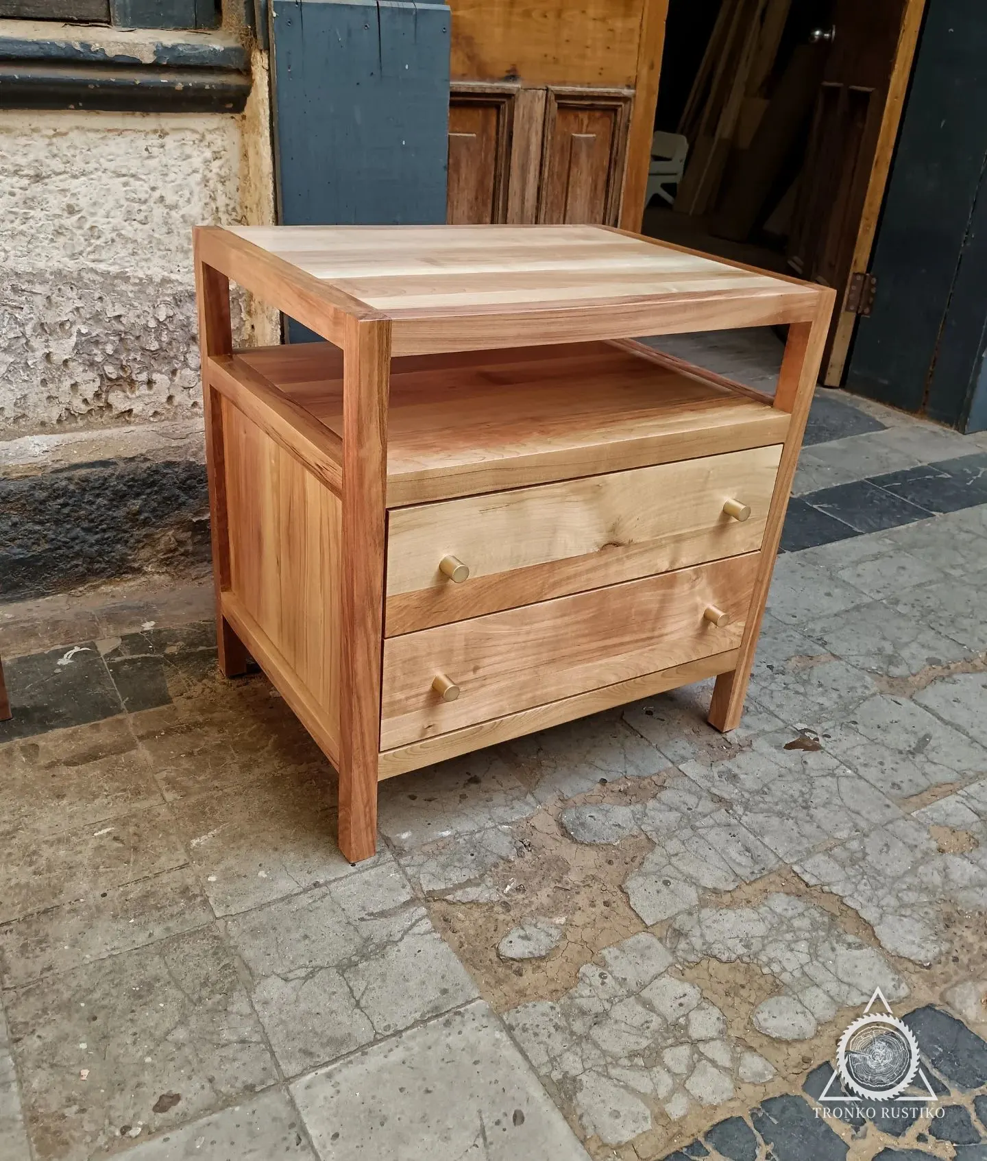 Velador de madera clara con estructura tipo marco, nicho superior y dos cajones.