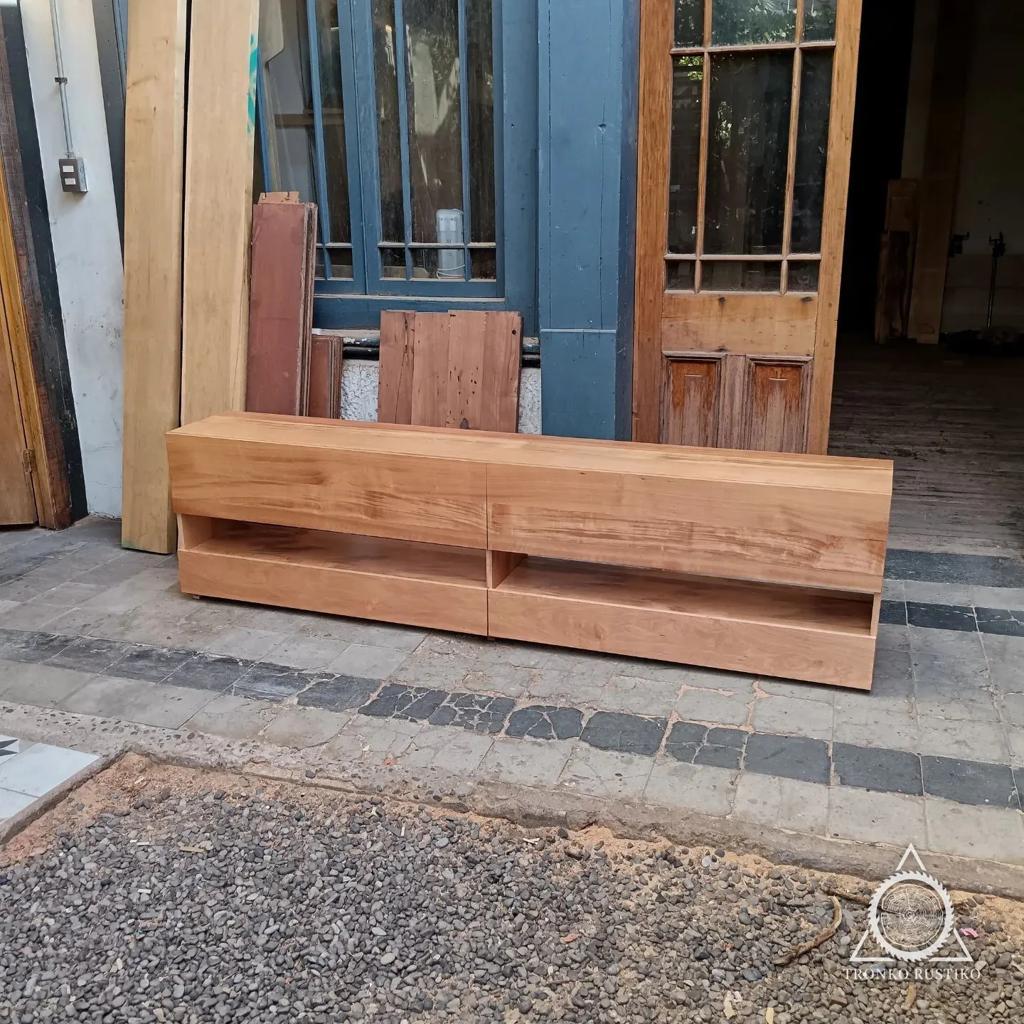 Rack bajo y largo de madera clara con nichos abiertos, apoyado en el suelo del taller.