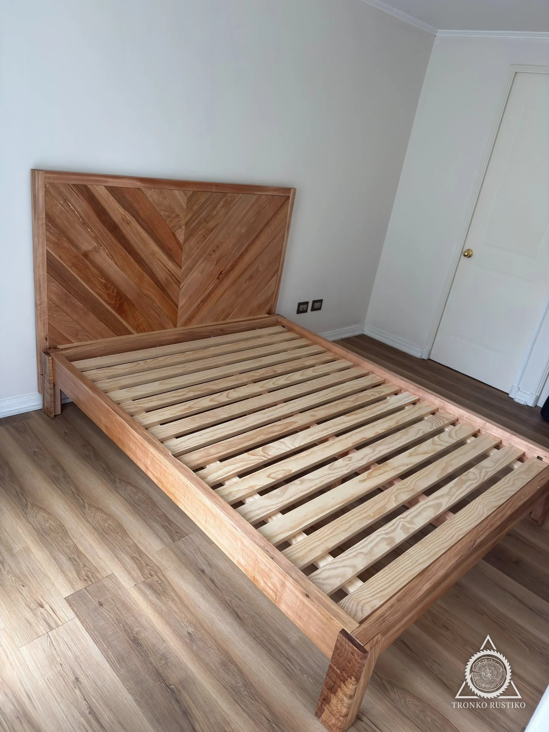 Cama de madera de dos plazas con respaldo de tablas en espiga y somier de listones, instalada en un dormitorio.