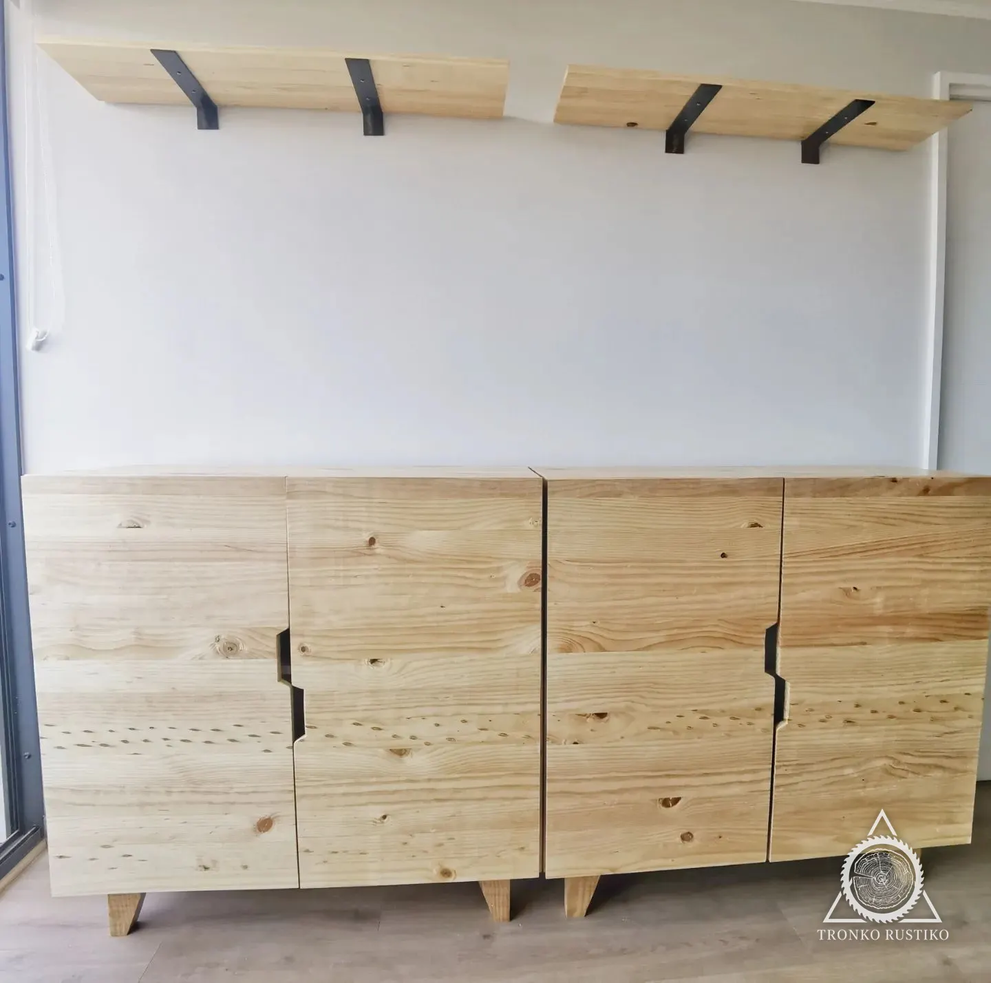 Arrimo largo de madera clara con cuatro puertas y tiradores negros, bajo unas repisas de muro.