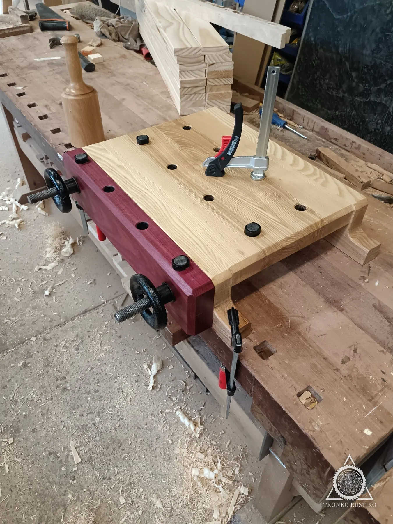 Prensa Moxon de madera clara con bloque frontal morado y ruedas de apriete, sobre el mesón del taller.