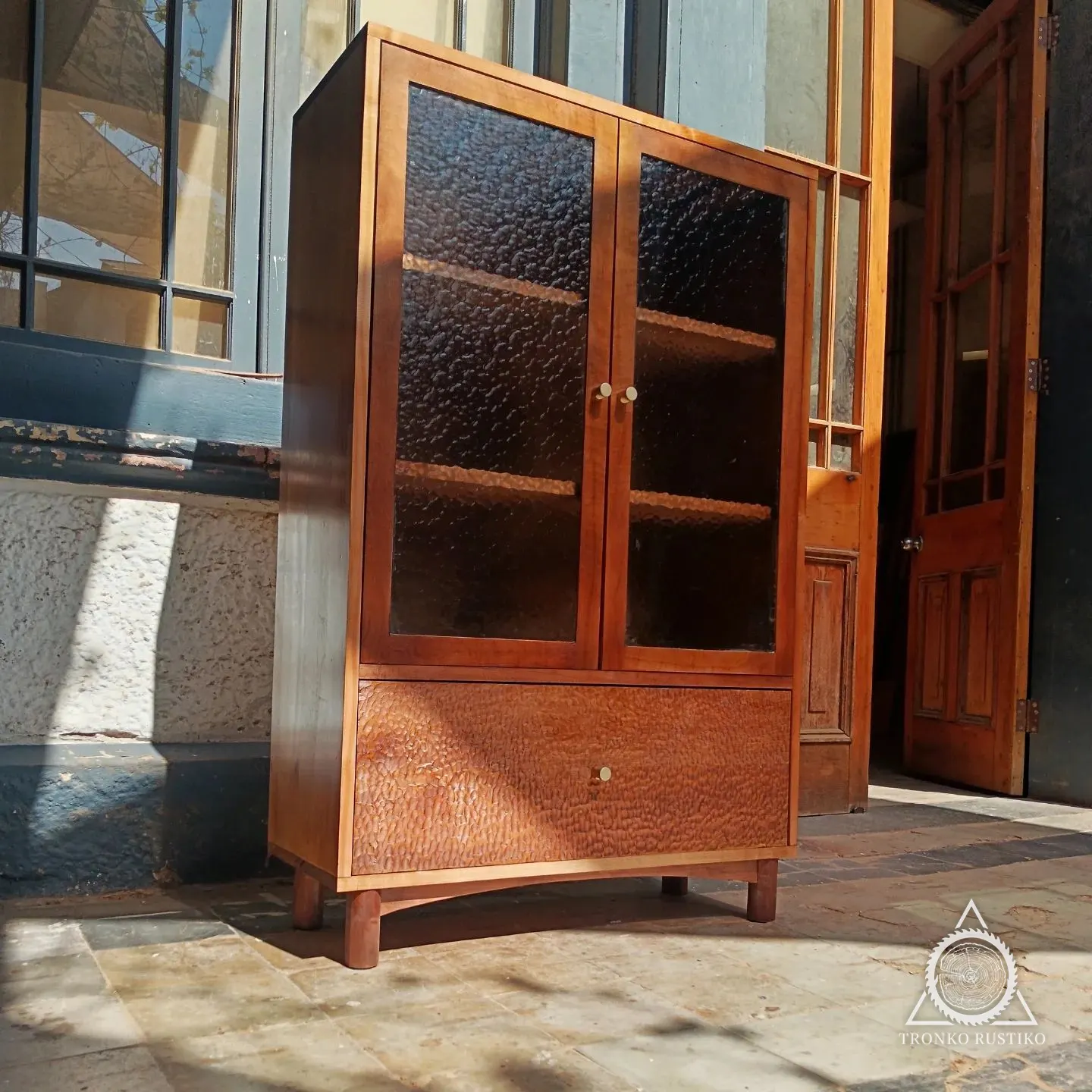 Vitrina de madera con puertas de vidrio martelé y cajón inferior texturizado.