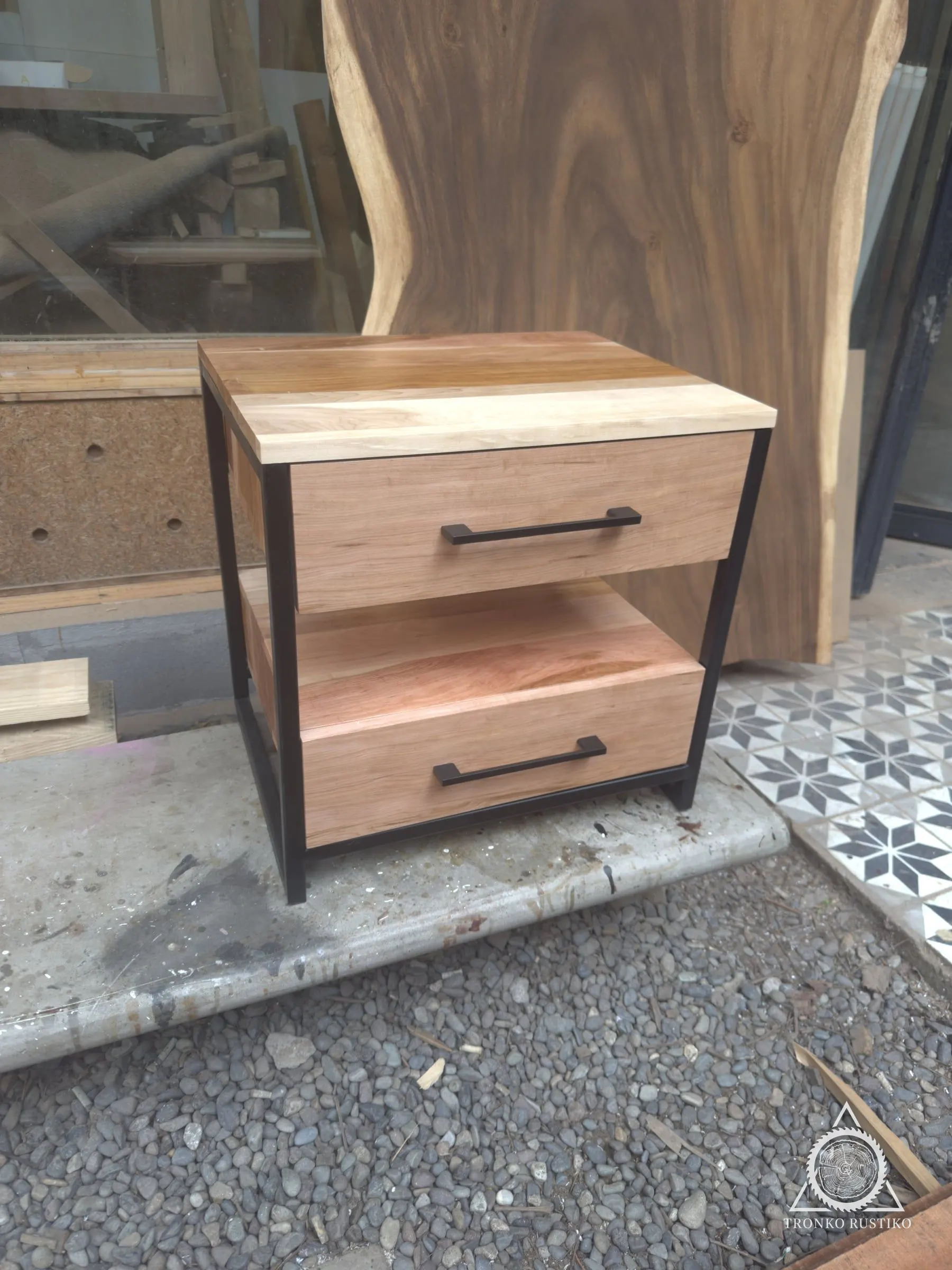 Velador de madera con estructura metálica negra y dos cajones con tiradores negros, en el taller.