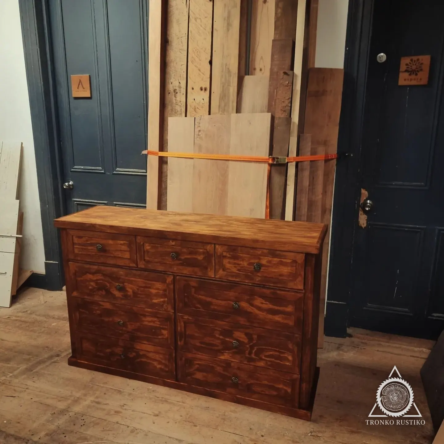Cómoda de madera teñida con marcos en los frentes y tiradores metálicos, en el taller.