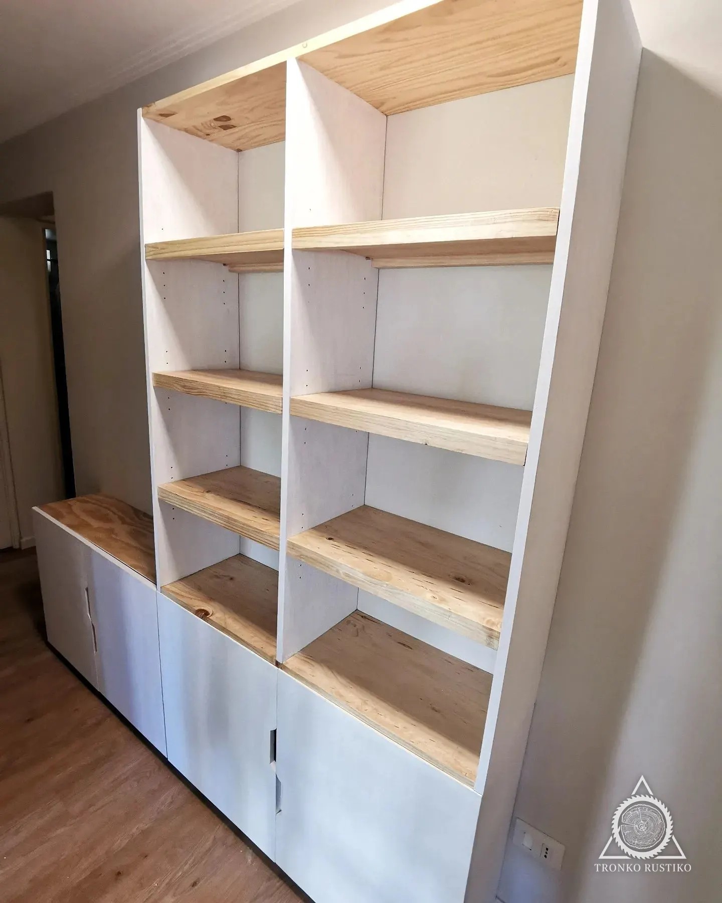 Librero blanco con repisas de madera natural y almacenamiento cerrado abajo.