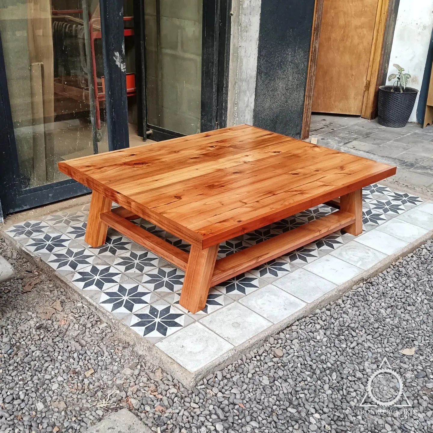 Mesa de centro de madera rojiza con cubierta gruesa, patas robustas y repisa inferior.