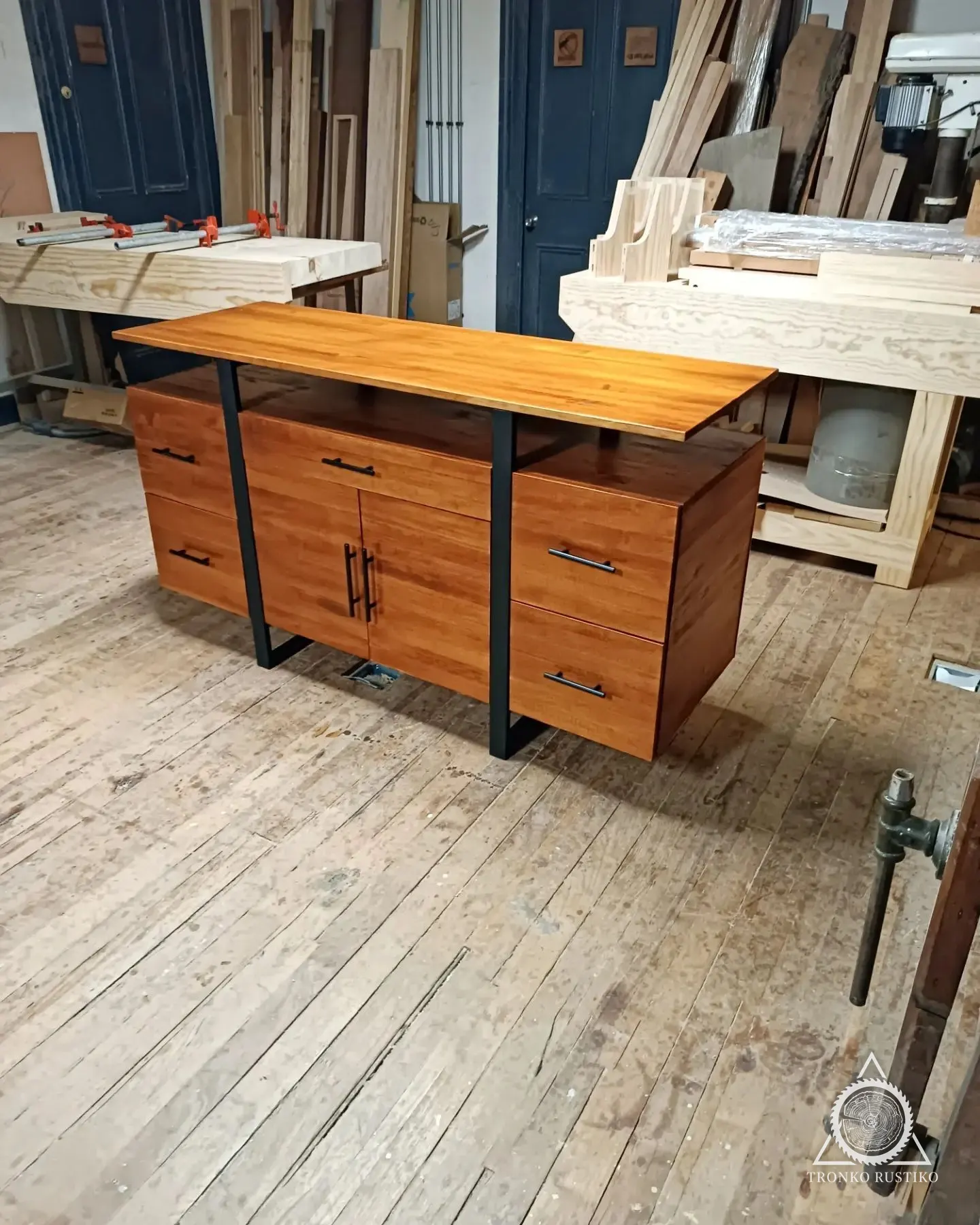 Rack alto de madera con estructura metálica negra, cajones laterales y puertas al centro, en el taller.