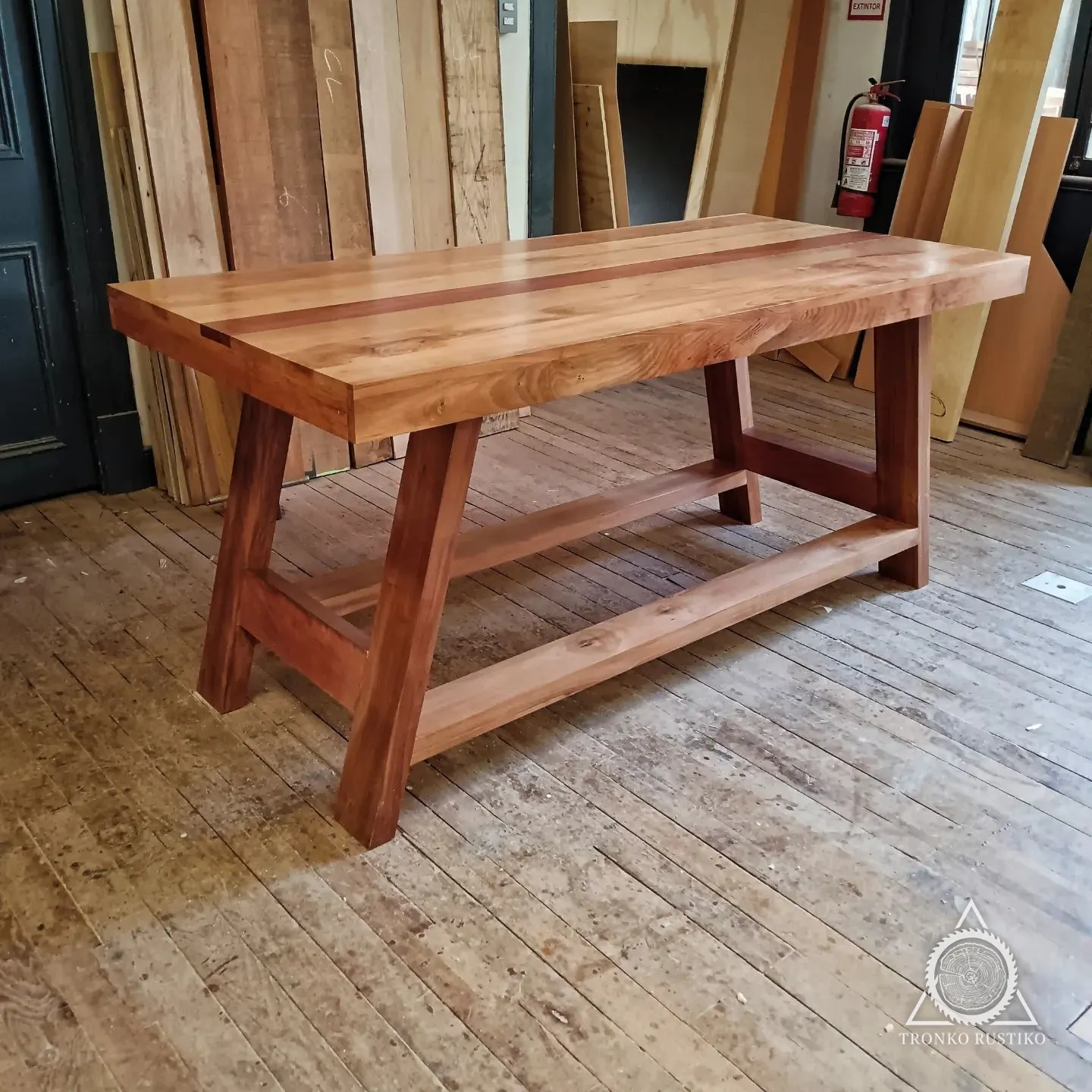 Mesa de comedor de madera con cubierta gruesa, patas tipo caballete y travesaño inferior.
